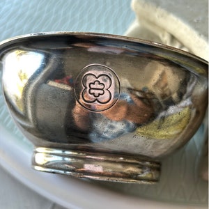 May include: A silver bowl with a floral design embossed on the bottom. The bowl has a slightly rounded shape and a smooth, reflective surface.