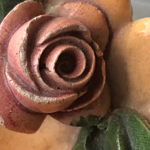 May include: A close-up of a carved wooden rose with a pink and brown color scheme. The rose is part of a larger decorative piece.