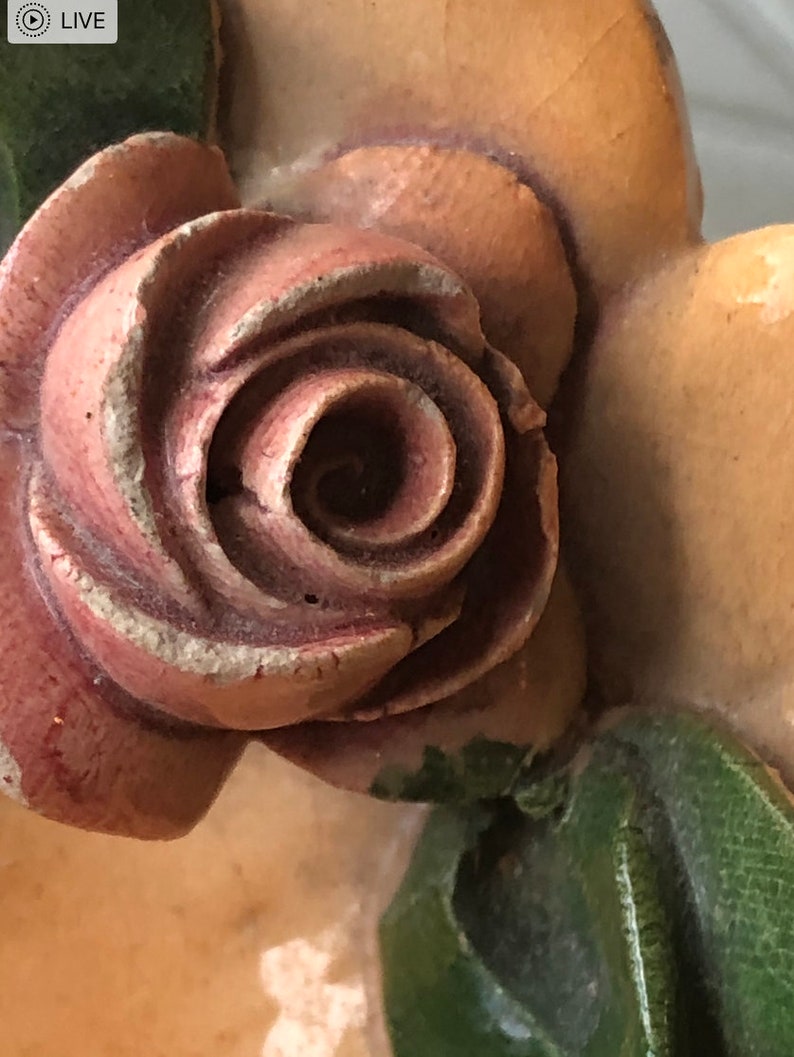 May include: A close-up of a carved wooden rose with a pink and brown color scheme. The rose is part of a larger decorative piece.