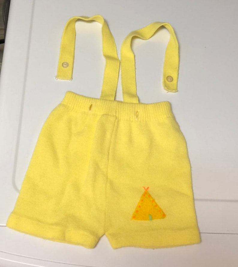 May include: Yellow knit shorts with suspenders and a small embroidered teepee design.