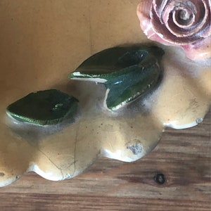 May include: A vintage ceramic trinket dish with a scalloped edge, featuring a pink rose and green leaves.