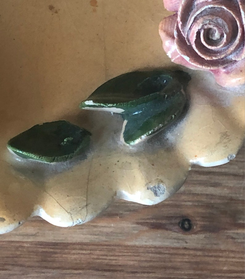 May include: A vintage ceramic trinket dish with a scalloped edge, featuring a pink rose and green leaves.