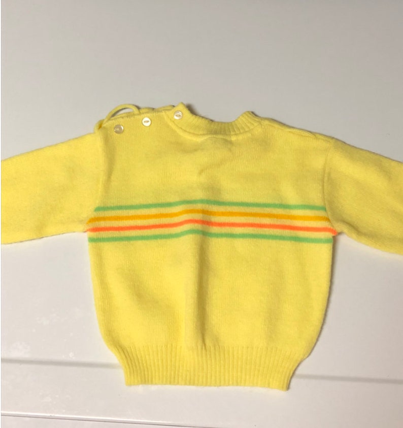 May include: A yellow knitted sweater with a striped pattern in green, orange, and pink.