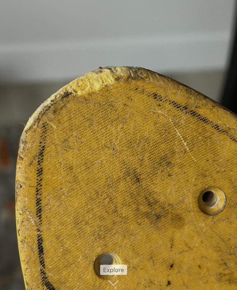 May include: Close-up of a yellow skateboard deck with two holes and a worn edge. The deck has a textured surface with black markings and the word "Explore" in a white box.