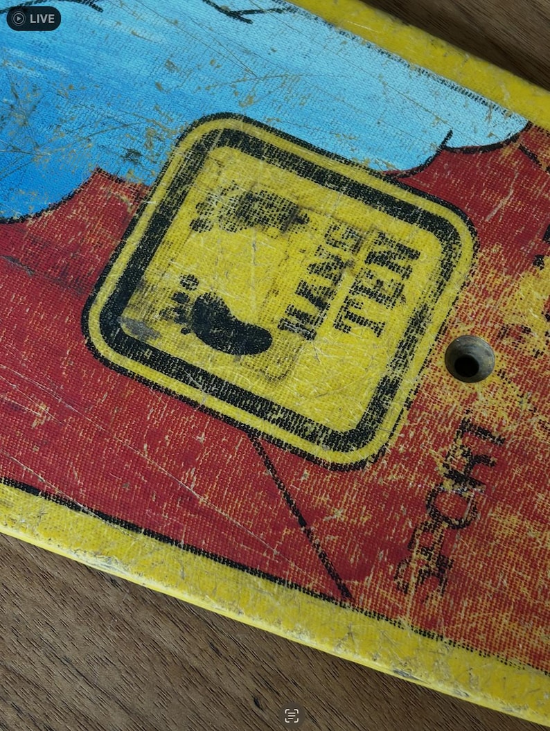 May include: Close-up of a vintage skateboard deck with a distressed finish. The deck features a yellow square with the text "HANG TEN" and a footprint graphic. The background has red and blue paint with visible wear and tear.