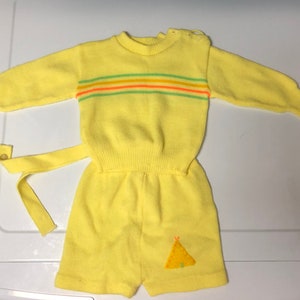 May include: Yellow knitted baby onesie with a striped pattern and a small embroidered teepee on the front.