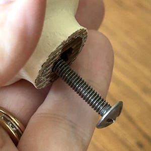 Peut inclure: Gros plan sur un bouton de meuble en bois avec une vis argent&eacute;e. Le bouton est de couleur beige clair et de forme cylindrique. La vis est fix&eacute;e au bouton et est en m&eacute;tal.