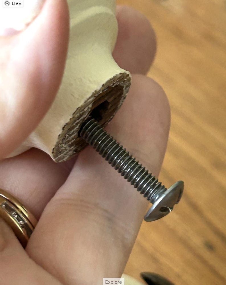 Peut inclure: Gros plan sur un bouton de meuble en bois avec une vis argent&eacute;e. Le bouton est de couleur beige clair et de forme cylindrique. La vis est fix&eacute;e au bouton et est en m&eacute;tal.