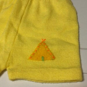May include: Yellow knit shorts with a felt applique of a yellow tent with orange and green details.