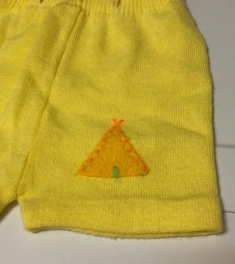 May include: Yellow knit shorts with a felt applique of a yellow tent with orange and green details.