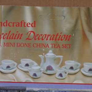 May include: A miniature white porcelain tea set with a floral design. The set includes a teapot, sugar bowl, creamer, cups, and saucers. The box reads "Handcrafted Porcelain Decoration 13pcs. MINI BONE CHINA TEA SET."