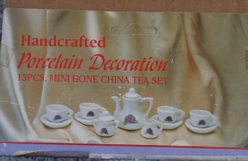 May include: A miniature white porcelain tea set with a floral design. The set includes a teapot, sugar bowl, creamer, cups, and saucers. The box reads "Handcrafted Porcelain Decoration 13pcs. MINI BONE CHINA TEA SET."