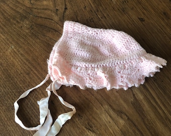 May include: A pink crocheted baby bonnet with a white satin ribbon tie.