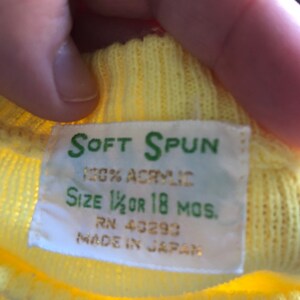 May include: Yellow knit sweater with a white tag that reads "SOFT SPUN 100% ACRYLIC SIZE 1 1/2 OR 18 MOS. RN 40293 MADE IN JAPAN"
