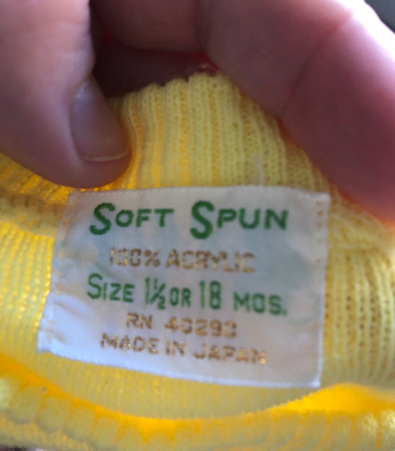 May include: Yellow knit sweater with a white tag that reads "SOFT SPUN 100% ACRYLIC SIZE 1 1/2 OR 18 MOS. RN 40293 MADE IN JAPAN"