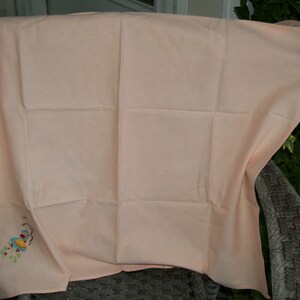May include: A peach-colored tablecloth with a small embroidered design of a flower and a bird.