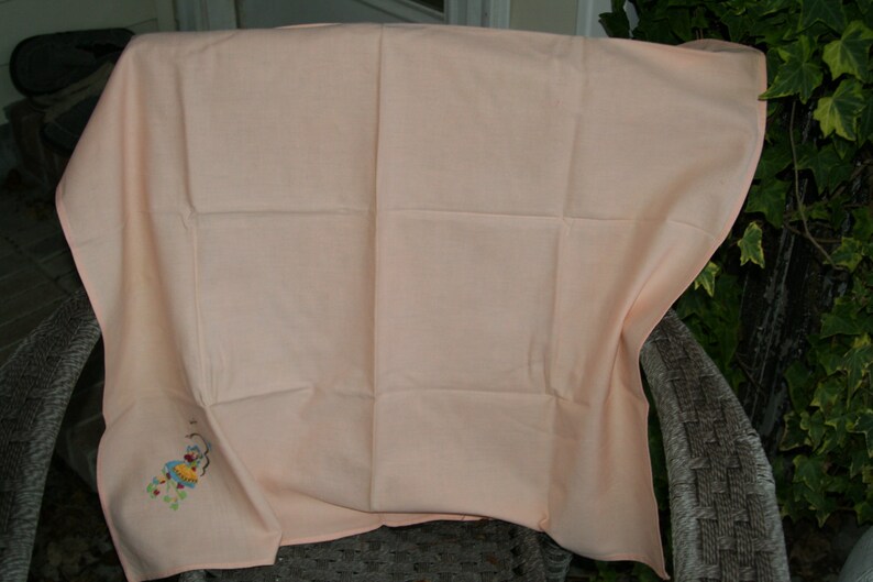 May include: A peach-colored tablecloth with a small embroidered design of a flower and a bird.