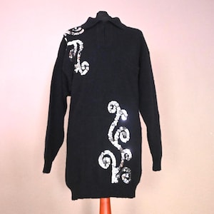 Può includere: Abito in maglia nero con decorazioni di paillettes bianche a forma di vortice. L'abito ha un collo e maniche lunghe. Le paillettes sono disposte in un disegno decorativo sul davanti.