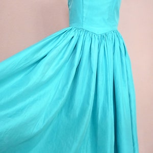 Peut inclure: Une robe turquoise sans bretelles avec un corsage ajust&eacute; et une jupe ample. La robe est faite d'un tissu lisse et soyeux.