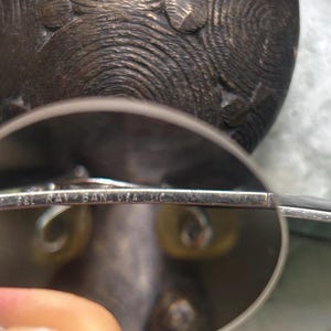 Puede incluir: Gafas de sol con montura plateada y lentes de color verde. El texto "B&L RAY-BAN USA" est&aacute; grabado en la montura. Las gafas de sol est&aacute;n colocadas delante de un objeto texturizado de color oscuro.