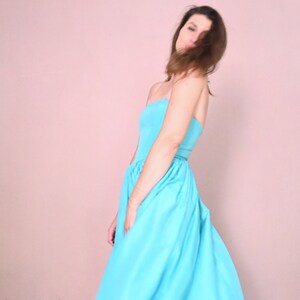 Peut inclure: Une femme portant une robe bleu clair sans bretelles. La robe est fluide et a une jupe pliss&eacute;e.