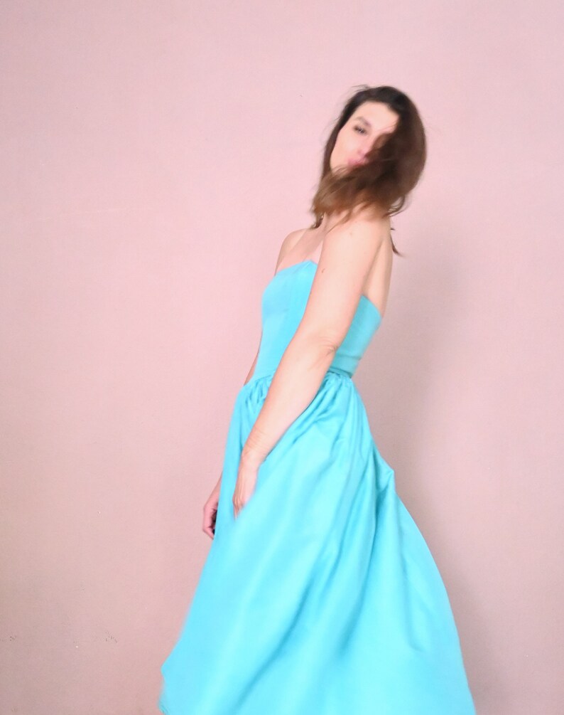 Peut inclure: Une femme portant une robe bleu clair sans bretelles. La robe est fluide et a une jupe pliss&eacute;e.