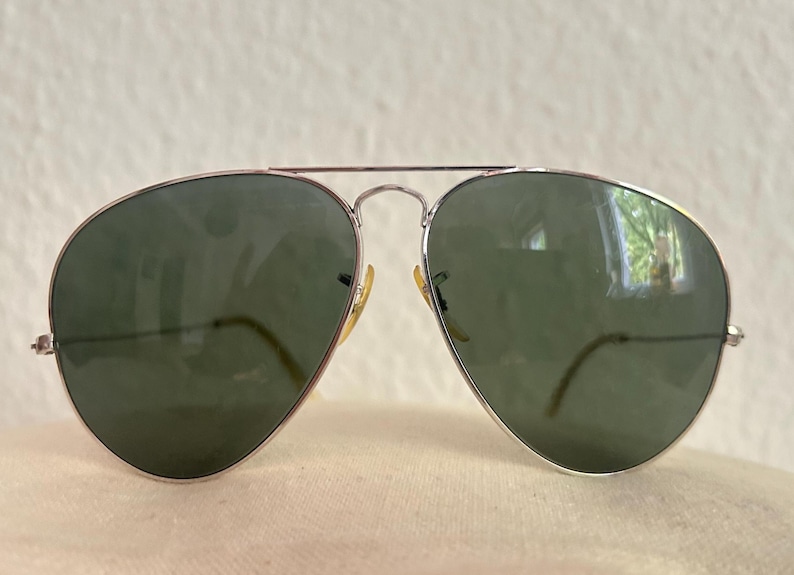 Puede incluir: Gafas de sol estilo aviador con montura de metal plateado y lentes verdes. Las lentes en forma de l&aacute;grima est&aacute;n engastadas en una montura fina plateada con doble puente. Las patillas son finas y curvadas. Un accesorio cl&aacute;sico.