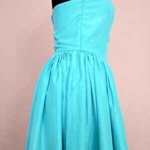 Peut inclure: Une robe turquoise sans bretelles avec une jupe pliss&eacute;e. La robe est sur un mannequin.