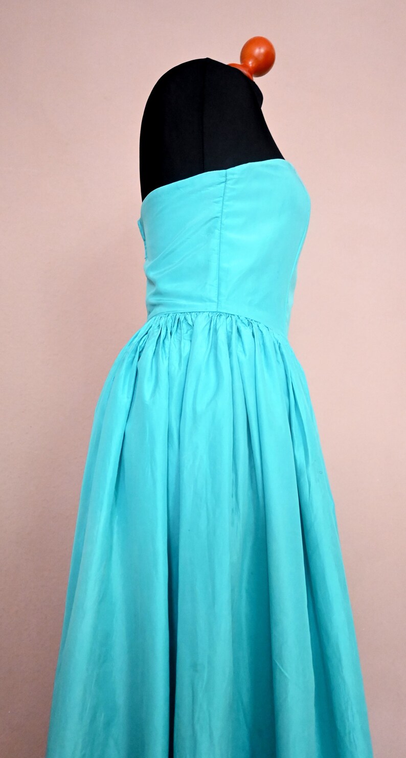 Peut inclure: Une robe turquoise sans bretelles avec une jupe pliss&eacute;e. La robe est sur un mannequin.