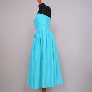 Peut inclure: Une robe turquoise sans bretelles avec un corsage ajust&eacute; et une jupe ample et fluide. La robe est faite d'un tissu lisse et soyeux.