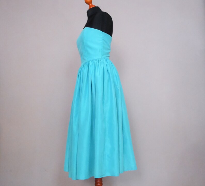 Peut inclure: Une robe turquoise sans bretelles avec un corsage ajust&eacute; et une jupe ample et fluide. La robe est faite d'un tissu lisse et soyeux.