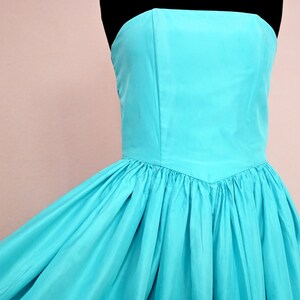 Peut inclure: Une robe turquoise sans bretelles avec un corsage ajust&eacute; et une jupe ample. La robe est faite d'un tissu lisse et soyeux.