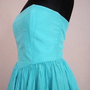 Peut inclure: Une robe turquoise sans bretelles avec un corsage ajust&eacute; et une jupe ample et pliss&eacute;e.