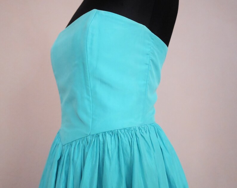 Peut inclure: Une robe turquoise sans bretelles avec un corsage ajust&eacute; et une jupe ample et pliss&eacute;e.