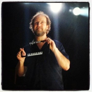 May include: A man wearing a black shirt with a black and white "PAGE SIDE" lanyard around his neck. He is holding a black and white keyboard in his left hand.