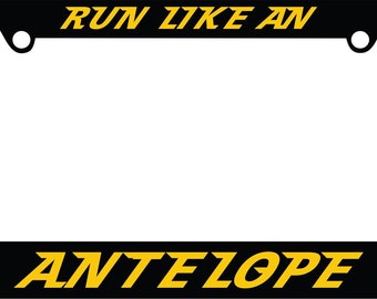Puede incluir: Marco de matrícula negro con texto amarillo que dice "RUN LIKE AN ANTELOPE" y dos siluetas amarillas de antílope corriendo en direcciones opuestas a cada lado del texto.