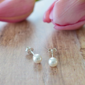 Peut inclure: Une paire de boucles d'oreilles en perles avec des tiges en argent. Les boucles d'oreilles sont sur une surface en bois avec des tulipes roses en arrière-plan.