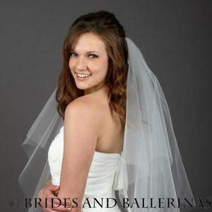 May include: A white strapless wedding dress with a ruched bodice and a sheer, multi-layered tulle veil. The text BRIDES AND BALLERINAS is visible across the lower portion of the image. The garment features a fitted silhouette and a back bow detail.