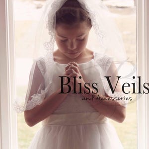 May include: A young girl wearing a white dress and a white lace veil with a white satin sash. She is praying with her hands clasped together. The image has the text "Bliss Veils and Accessories" at the bottom.