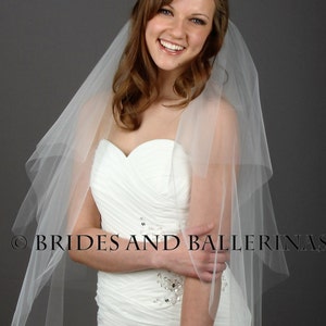 May include: A white strapless wedding dress with a sweetheart neckline and ruched bodice featuring silver sequin embellishments. A sheer, layered white tulle veil is draped over the shoulders. The text BRIDES AND BALLERINAS is visible.