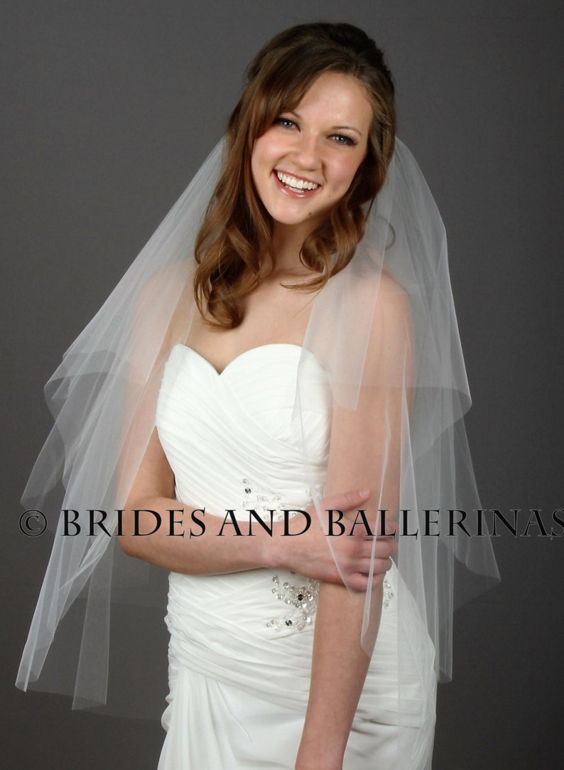 May include: A white strapless wedding dress with a sweetheart neckline and ruched bodice featuring silver sequin embellishments. A sheer, layered white tulle veil is draped over the shoulders. The text BRIDES AND BALLERINAS is visible.