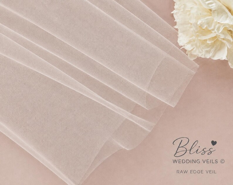 May include: A sheer, light blush-colored tulle veil with a raw edge. The fabric is folded in soft layers, creating a delicate texture. In the corner, the text reads: Bliss WEDDING VEILS &copy; RAW EDGE VEIL, accompanied by a small heart icon.