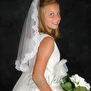 May include: A young person wearing a white dress and a white lace veil. They are holding a bouquet of white flowers.