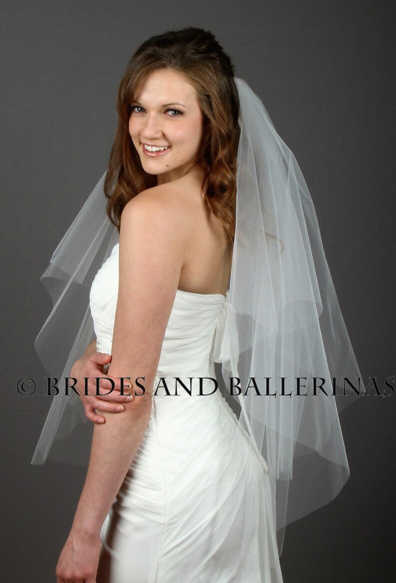 May include: A white strapless wedding dress with a ruched bodice and a sheer, multi-layered tulle veil. The text BRIDES AND BALLERINAS is visible across the lower portion of the image. The garment features a fitted silhouette and a back bow detail.