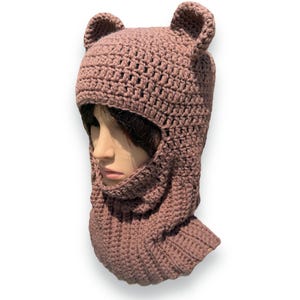 Peut inclure: Une cagoule en crochet mauve avec des rabats d'oreilles en forme d'oreilles d'ours.