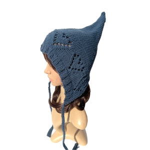 May include: A blue knitted hat with a pointed top and a lace pattern. The hat has long ties that can be tied under the chin.