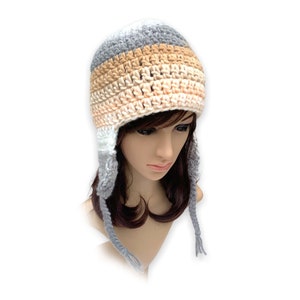 May include: A gray, beige, and white striped crocheted hat with ear flaps. The hat has a simple design and is made with soft yarn.