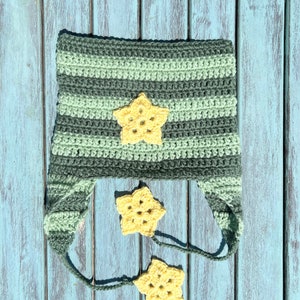 May include: A green and gray striped crocheted hat with a yellow star on top and two yellow stars hanging from the ties.