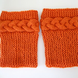 May include: A pair of orange knitted leg warmers with a cable knit design at the top.