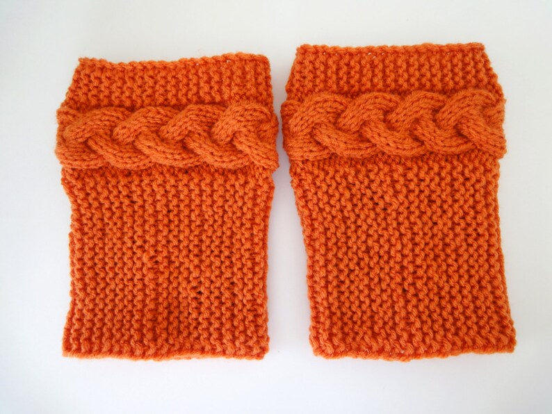May include: A pair of orange knitted leg warmers with a cable knit design at the top.